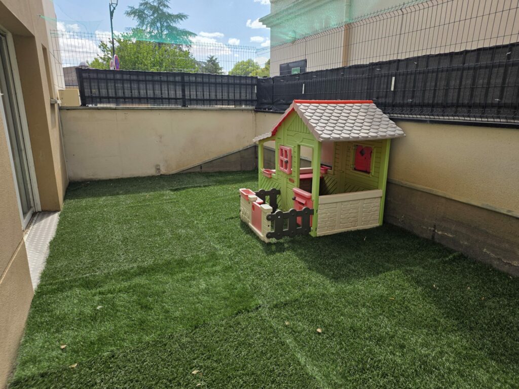 Espace extérieur de la micro crèche avec de la pelouse synthétique et une maisonnette pour enfants